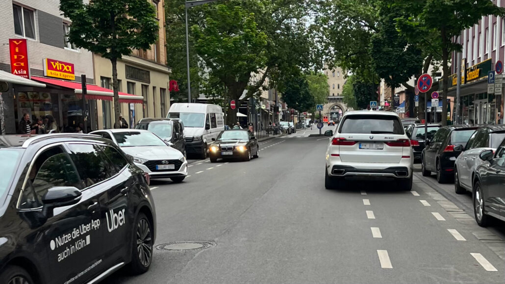 Auf einer Straße in Köln stehen viele große Autos auf den Fahrrad-Schutz-Streifen. Es wäre gefährlich, mit dem Fahrrad vorbei zu fahren.